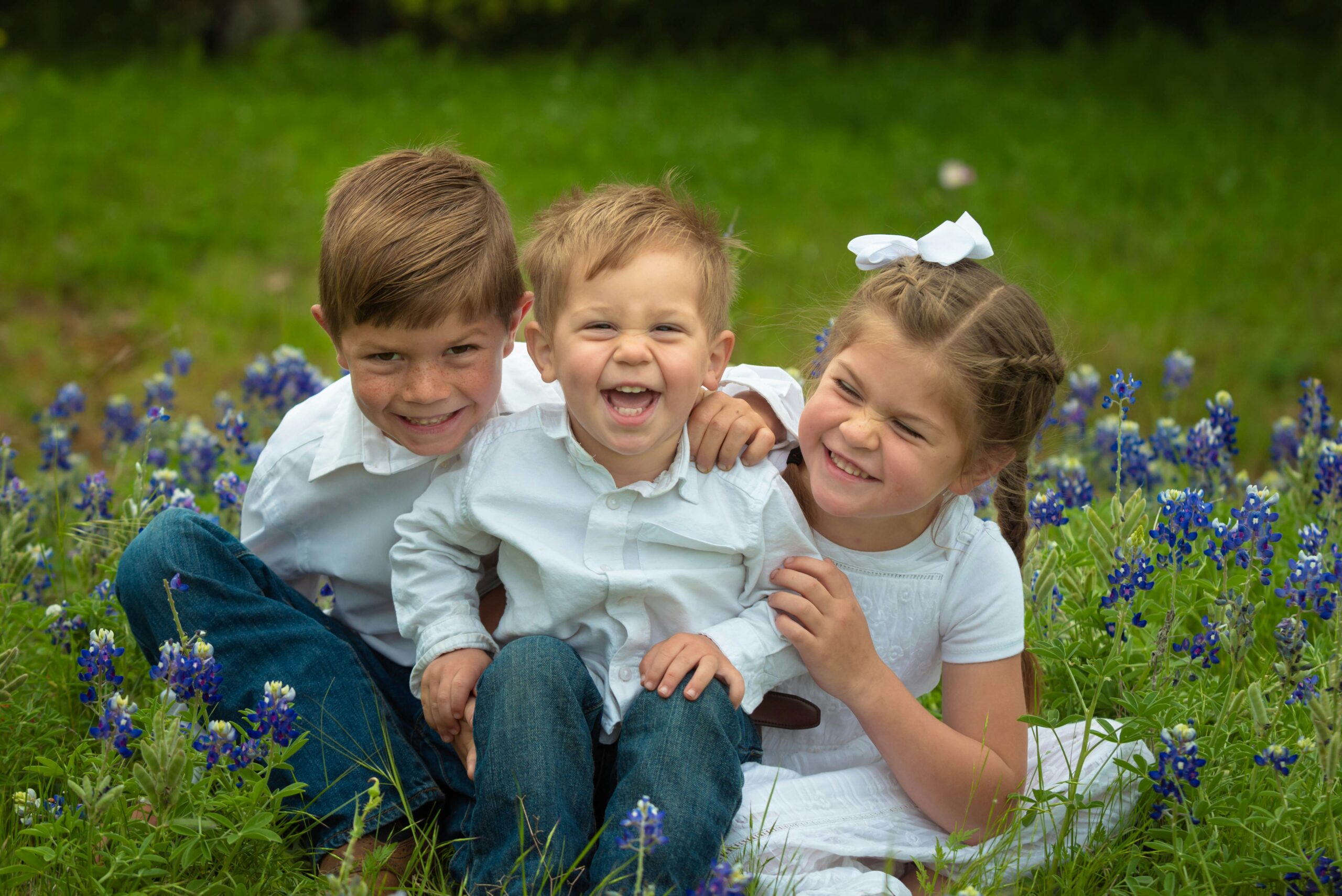 Three smiling children sitting in a field of bluebonnets, symbolizing joy, hope, and belonging in foster and adoptive families.